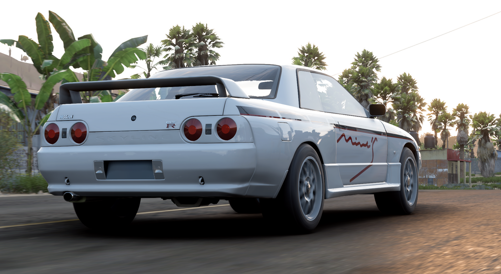 A white Nissan GT-R drives down a road past palm trees.