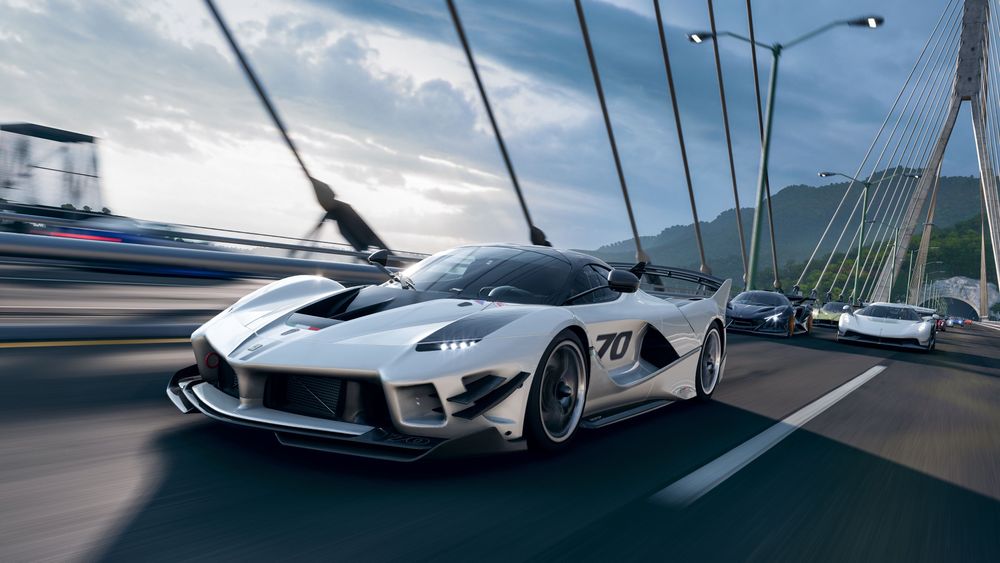 Ferrari FXX-K Evo speeding across a suspension bridge with other cars behind it.