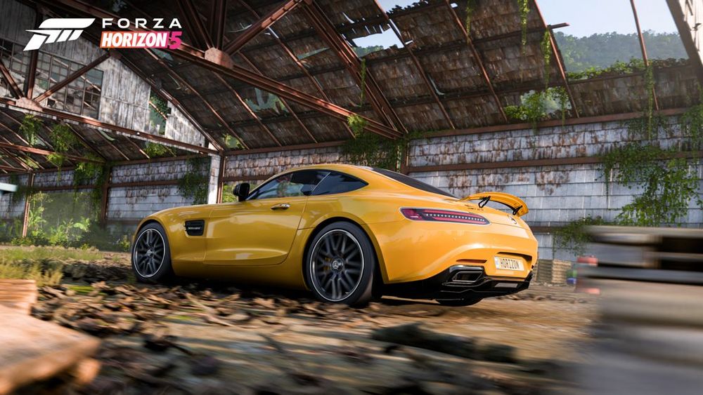 A yellow Mercedes AMG GT S drives through an abandoned airfield hangar.