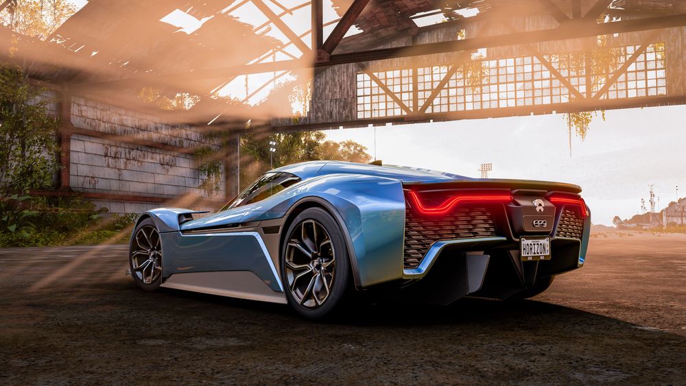 A blue NIO EP9 is parked in an abandoned airport hangar as sun rays shine through the openings.