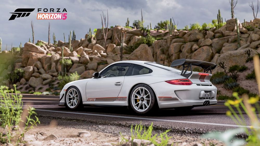 A white Porsche 911 GT3 surrounded by rocks is parked on a road by the desert.