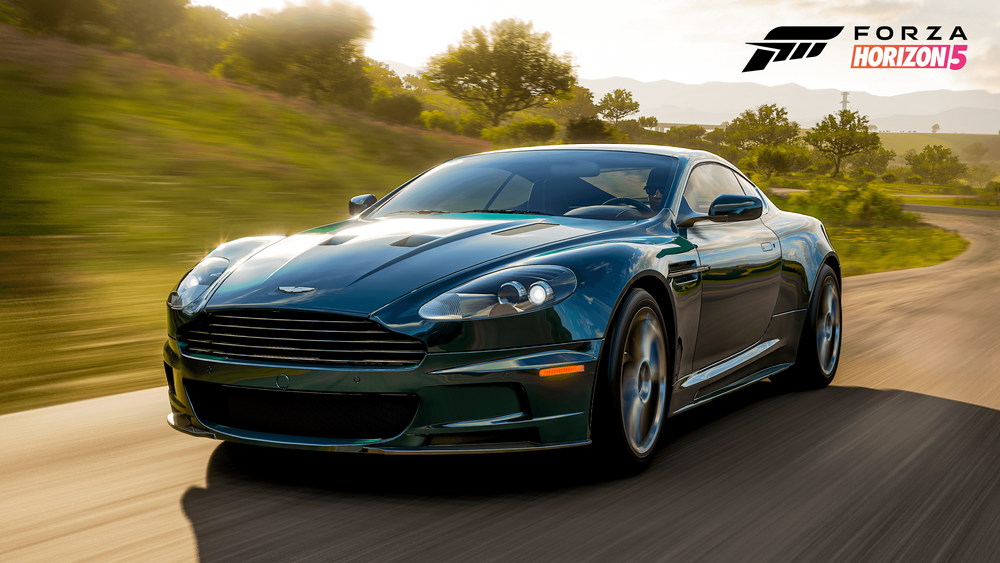 Aston Martin DBS running on an asphalt road in front of bushes and grass
