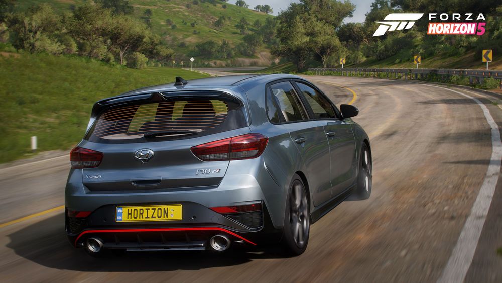 Gray hatchback about to take a left corner on a tarmac road covered in dirt