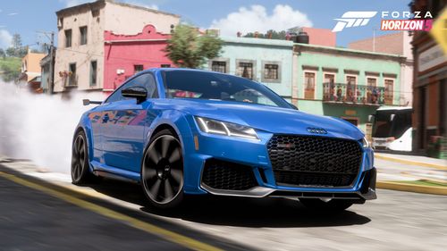 Audi TT RS taking a sharp turn on a stone road surrounded by houses