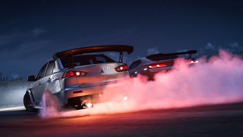 A pair of silver vehicles drifting together creating tons of tire smoke.