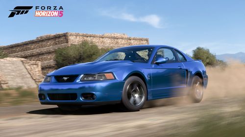 Mustang SVT driving on a dirt road in front of ancient ruins kicking dust as it passes