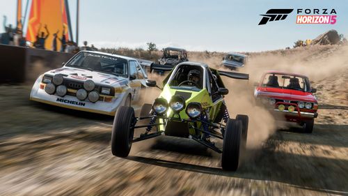 A group of off-road cars including a green buggy, red half-truck and white rally car drive along a dirt trail with spectators cheering on the action in the left side of the image.