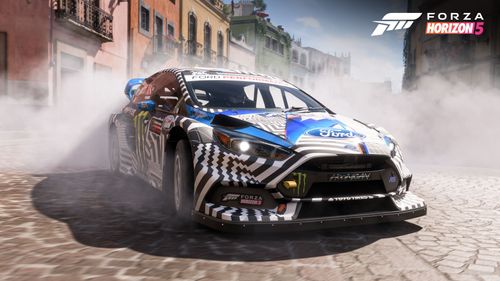 A Hoonigan GYMKHANA 9 Ford Focus RS RX with a black, white and blue livery featuring a green Monster Energy logo lifts some tire smoke drifting around the city of Guanajuato.