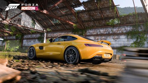 A yellow Mercedes AMG GT S drives through an abandoned airfield hangar.