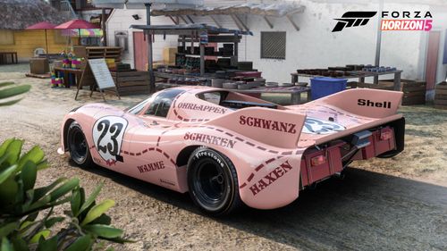 The rear view of a Porsche 917 "pink pig" race car parked in a Mexican seaside town.