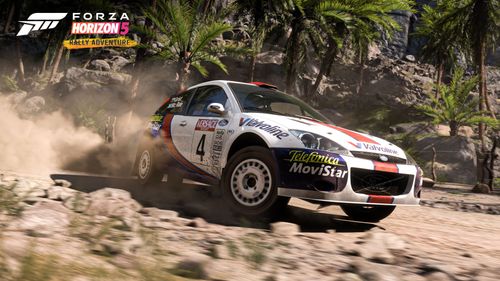 Colin McRae's Ford Focus RS kicks up dust with smashable palm trees and rocky terrain in the background.