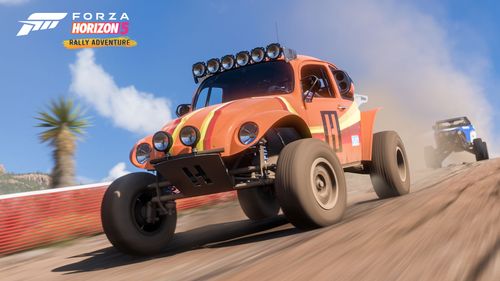 A Volkswagen Baja Beetle with a Hoonigan orange striped livery drives in front of a blue buggy on a dirt trail with a clear blue sky in the background.