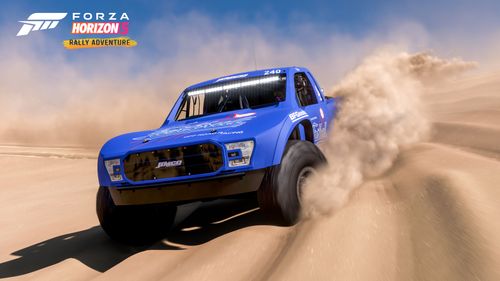 A Jimco truck sporting a blue Fastball Racing livery kicks up dust and leaves behind tire tracks in the deformable sand dunes.