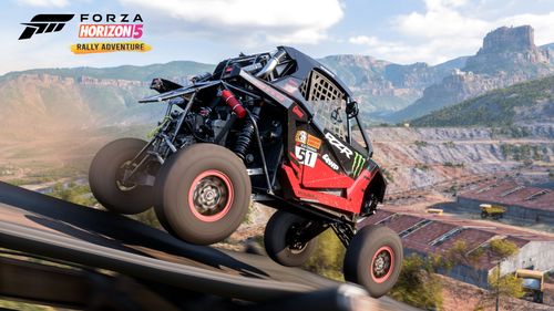 A black and red Polaris RZR Pro XP Factory Racing buggy drives towards some abandoned warehouses in the quarry.