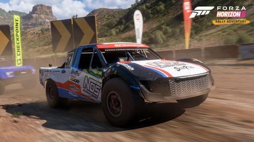 A RJ Anderson truck with a white, blue and red livery races on a dirt trail, closely followed by a blue Jimco truck.