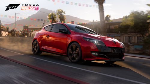 Side view of red Renault Megane RS 250 as it drives by seaside town buildings.