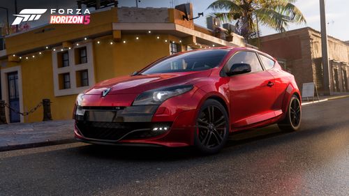 Side view of red Renault Megane RS 250 parked by seaside town buildings.