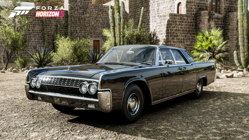 Black Lincoln Continental parked outdoors in front of cacti and a brick wall