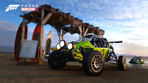 A green 2021 SIERRA Cars 700R buggy parked on the beach alongside three surf boards, two red, one white, leaning up against a beach hut. A green and black jet ski can also be seen in the water.