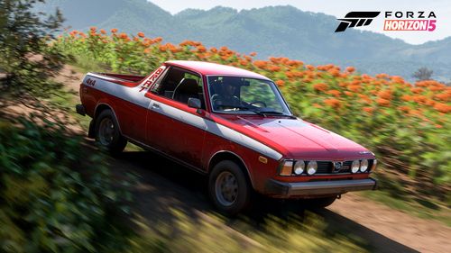 The 1980 Subaru BRAT GL in its red and white livery drives through a field of orange flowers.