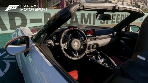 A FIAT 124 Spider with its top down parked inside a raceway looking into a wall