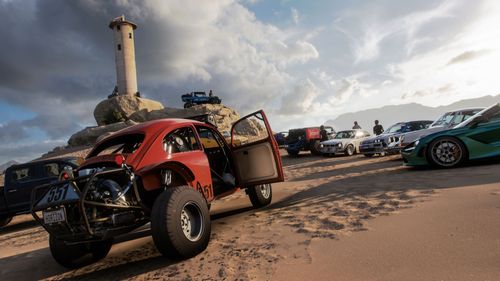 Several cars parked in a sandy area under a light tower.