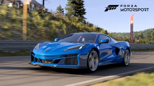 2024 Chevrolet Corvette E-Ray in blue. The car is moving quickly on a racing circuit that is lined with grass just beyond the edge of the track and a metallic barrier a little bit beyond the grass.